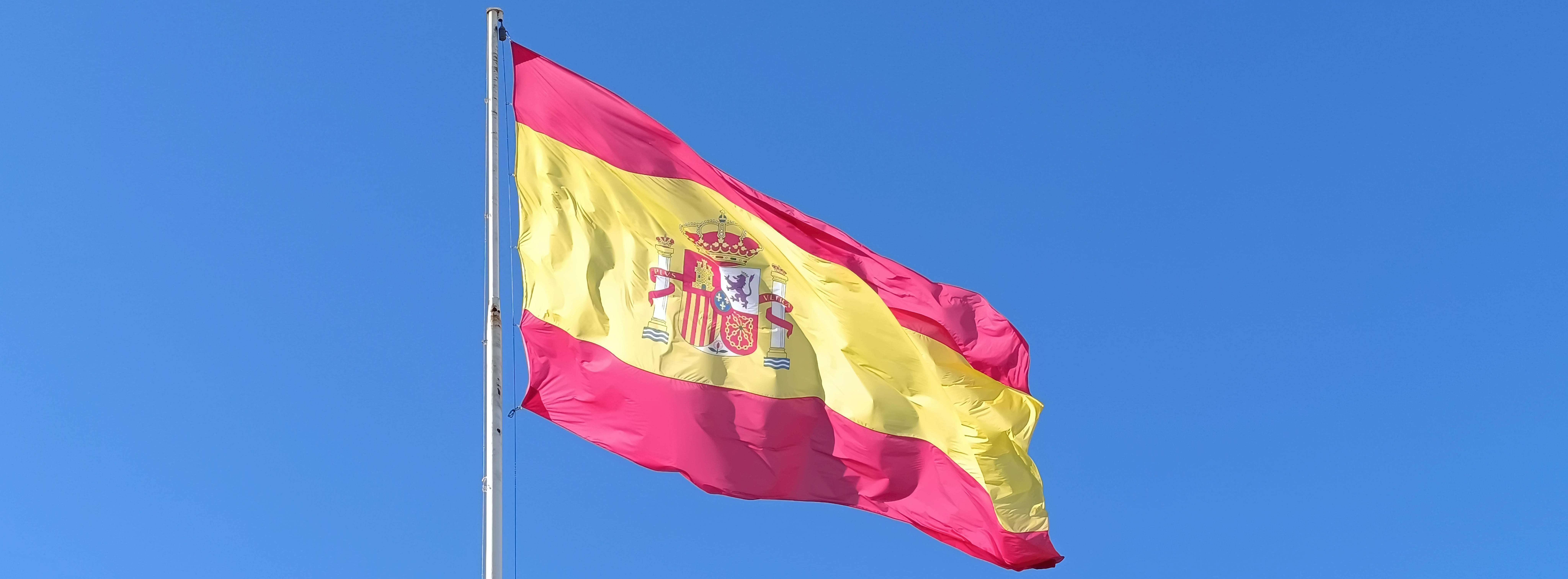 Spanish flag on a pole fluttering in the wind against a blue sky