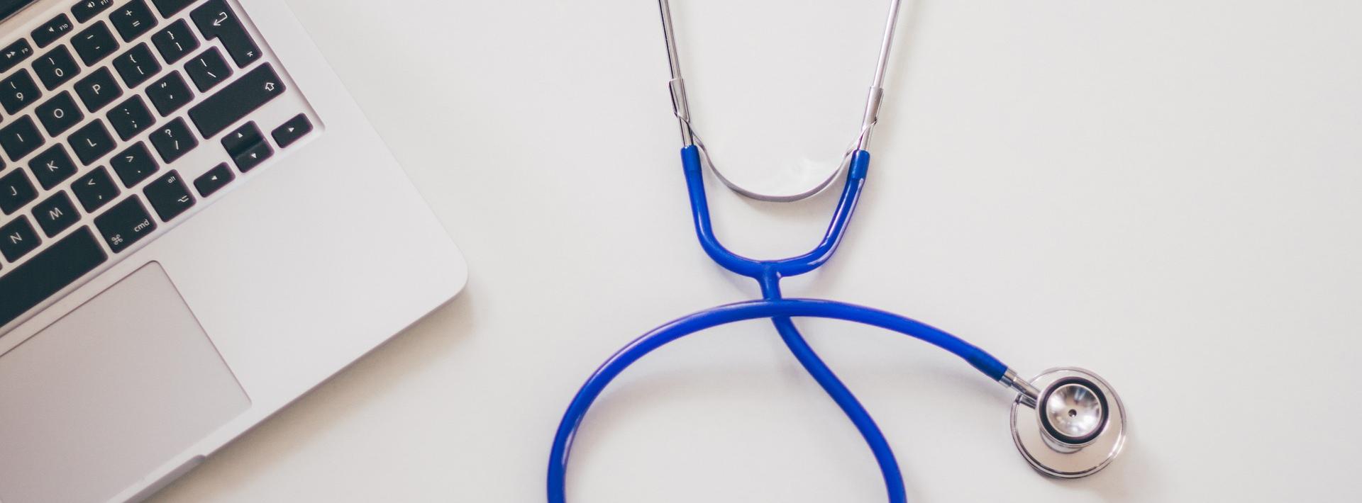 Stethoscope and laptop on a grey desk