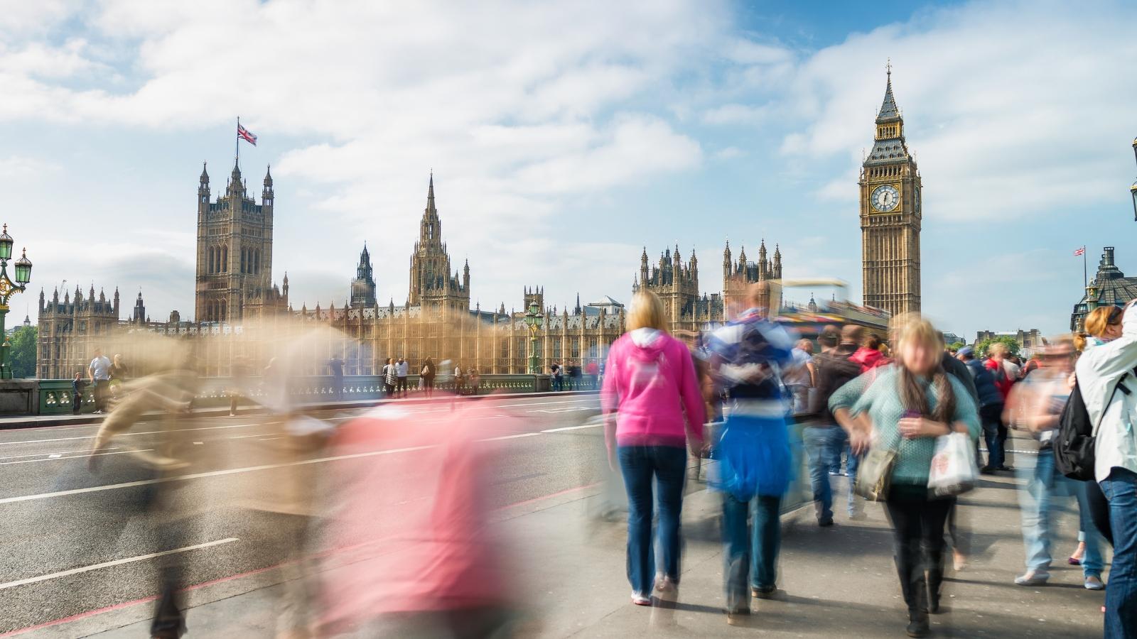 A busy crowd of pedestrians on Westminster Bridge in London, with the Houses of Parliament and Big Ben behind them.