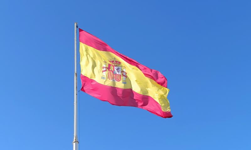 Spanish flag on a pole fluttering in the wind against a blue sky