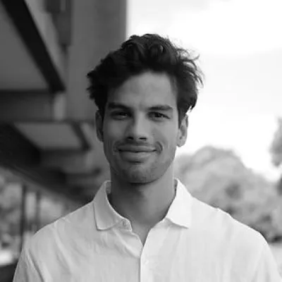 Arun wears a white button down shirt and has dark hair.