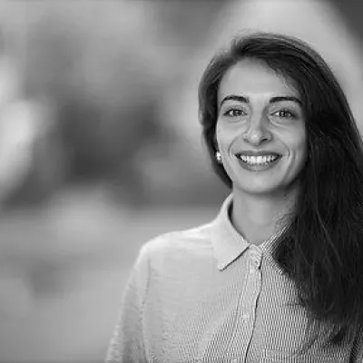 Giverna has long dark hair, is wearing a buttoned up shirt and smiles.
