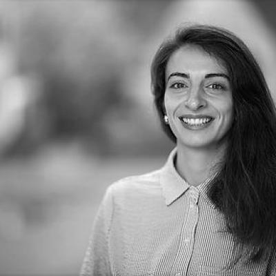 Giverna has long dark hair, is wearing a buttoned up shirt and smiles.