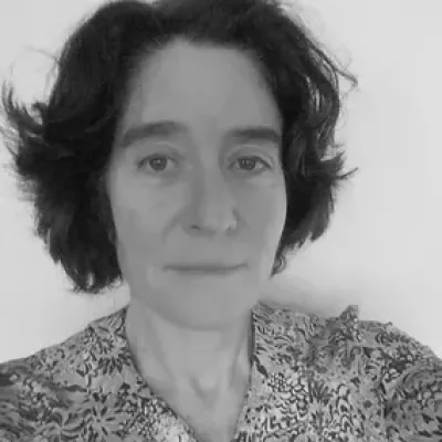 Romola has short dark hair and looks into the camera.